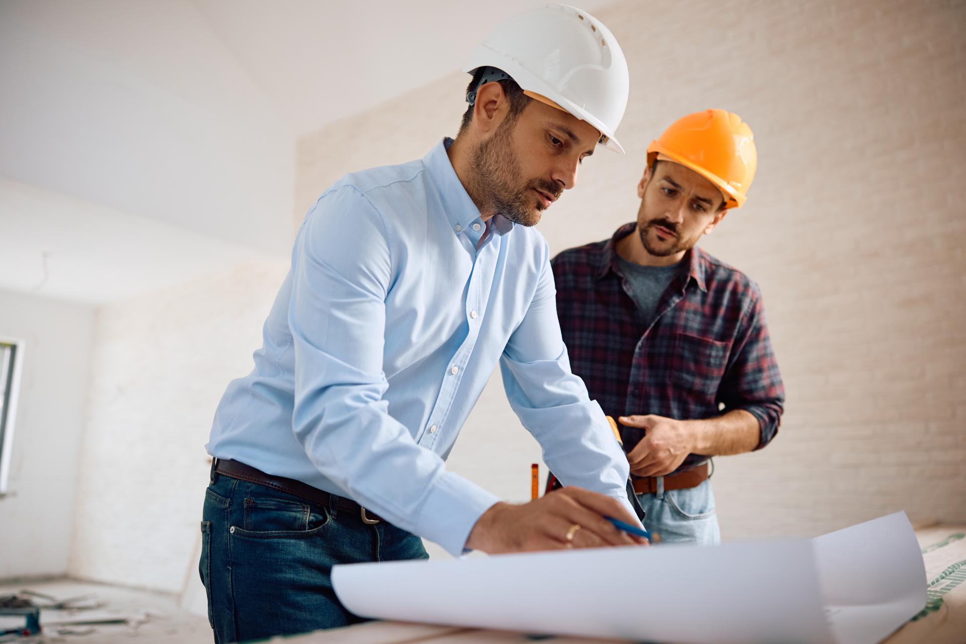 Architect and construction worker analyzing blueprints during home remodeling project.